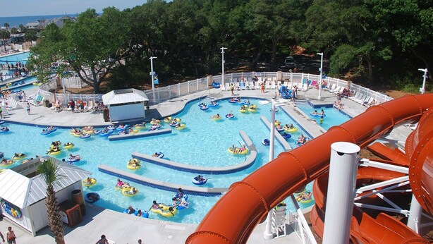 Un parco acquatico con diverse piscine, zattere gonfiabili e un grande scivolo d'acqua.