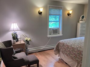A bedroom with a bed, a chair, a lamp, a vase with flowers, a dresser, and two wall-mounted lights. - Hall of Fame Hide Away (Richfield Springs)
