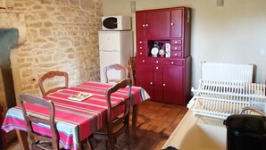 A kitchen with a stone wall, a red cabinet with drawers, a white refrigerator, and a dining table with chairs. - Gite aux Portes du Morvan, 10 minutes from Vézelay (Nuars)