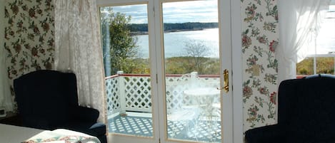 A room with a bed, two chairs, a table, and a view of a lake through a glass door.
