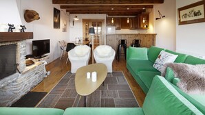 Un salon chaleureux avec un canapé vert, une cheminée, un téléviseur et un coin repas comprenant des chaises et une table.