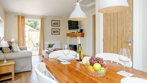 A dining area with a wooden table, white chairs, a fruit bowl, wine glasses, and a television on a shelf. - 1 bedroom accommodation in Roughton, near Woodhall Spa (Roughton, near Woodhall Spa)