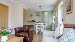 A living room with a brown leather chair, a white sofa with plaid cushions, a wooden table, and a vase of flowers. - 1 bedroom accommodation in Roughton, near Woodhall Spa (Roughton, near Woodhall Spa)