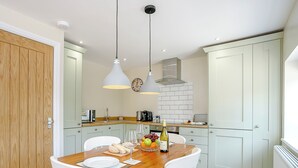 A dining area with a wooden table, white chairs, and a fruit bowl. - 1 bedroom accommodation in Roughton, near Woodhall Spa (Roughton, near Woodhall Spa)