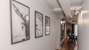 A hallway with framed artwork on the walls, wooden flooring, and a dining area with chairs and a table.