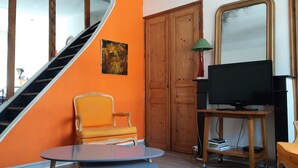 A room with a staircase, orange walls, a wooden door, a television on a stand, a table, and two chairs. - Bright Duplex in Lille-Wazemmès (Lille)