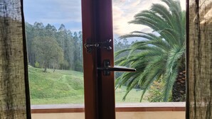 A wooden balcony with a view of a green landscape and palm trees.