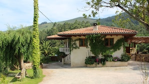 A house with a tiled roof, surrounded by greenery and a gravel driveway.
