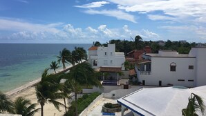 A coastal view with a beach, palm trees, and buildings with a white facade and red roofs. - Beach Front Penthouse on the Beach (Puerto Morelos)