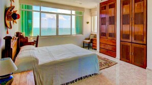 A bedroom with a bed, a desk, a chair, a wardrobe, and a window with a view of the sea. - Beach Front Penthouse on the Beach (Puerto Morelos)