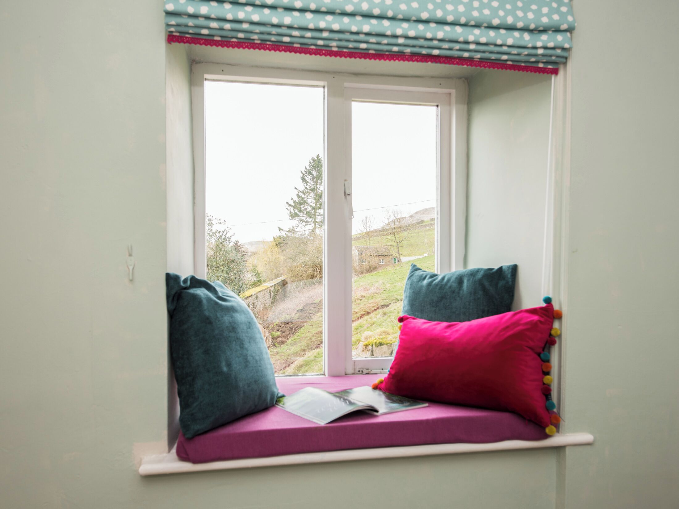 A window seat with cushions and a book.