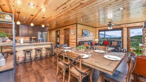 Interior de una cabaña de madera con comedor, cocina y zona de estar con vistas.