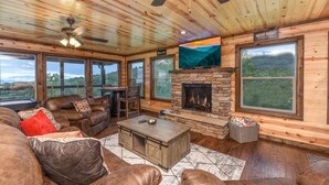 Un salón acogedor con sofás de cuero, una chimenea de piedra y amplias ventanas con vistas panorámicas.