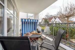 Een balkon met een tafel, stoelen, een gestreept gordijn en uitzicht op huizen en bomen.
