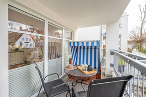 Een balkon met een tafel, stoelen en een geruit gordijn.