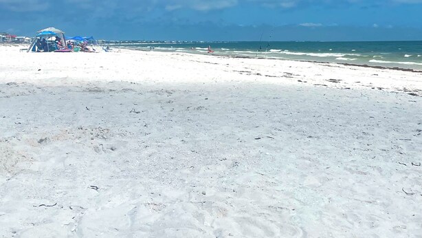 A beach with a clear sky and a few clouds. There is a structure with blue and white colors in the background. - Cozy Coastal Condo – Walk to Beach, Dine, & Relax! (Mexico Beach)