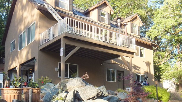 Une maison à deux étages avec un balcon, de gros rochers et un étang.