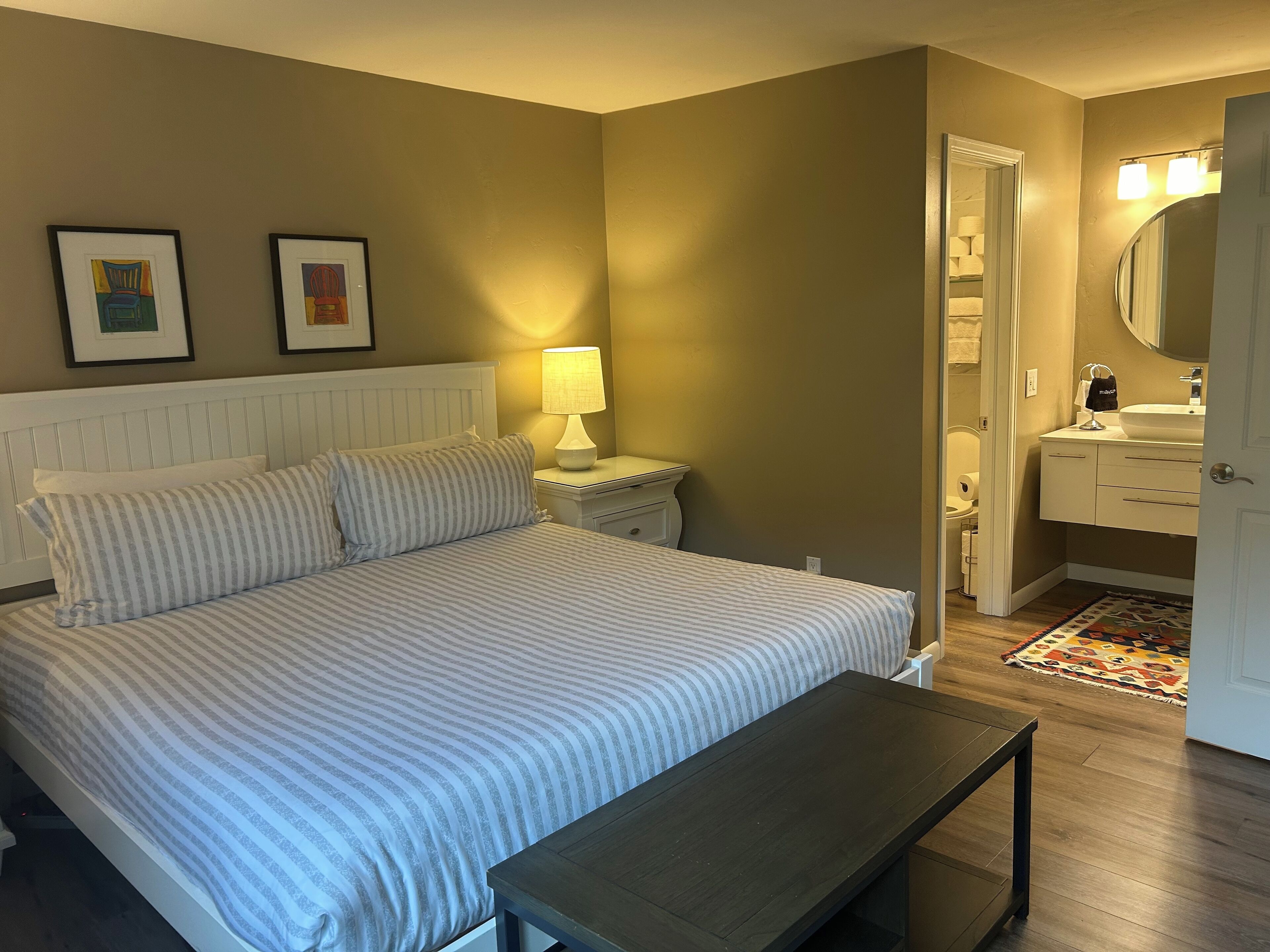 Une chambre à coucher avec un lit, une table de chevet, une lampe et un banc.