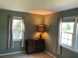 Une pièce avec deux fenêtres, une commode en bois et une lampe fixée au mur.