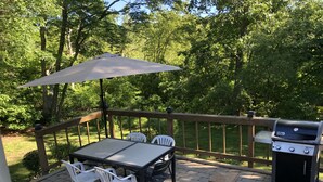 Un patio exterior con una mesa y sillas, una parrilla y barandilla de madera.