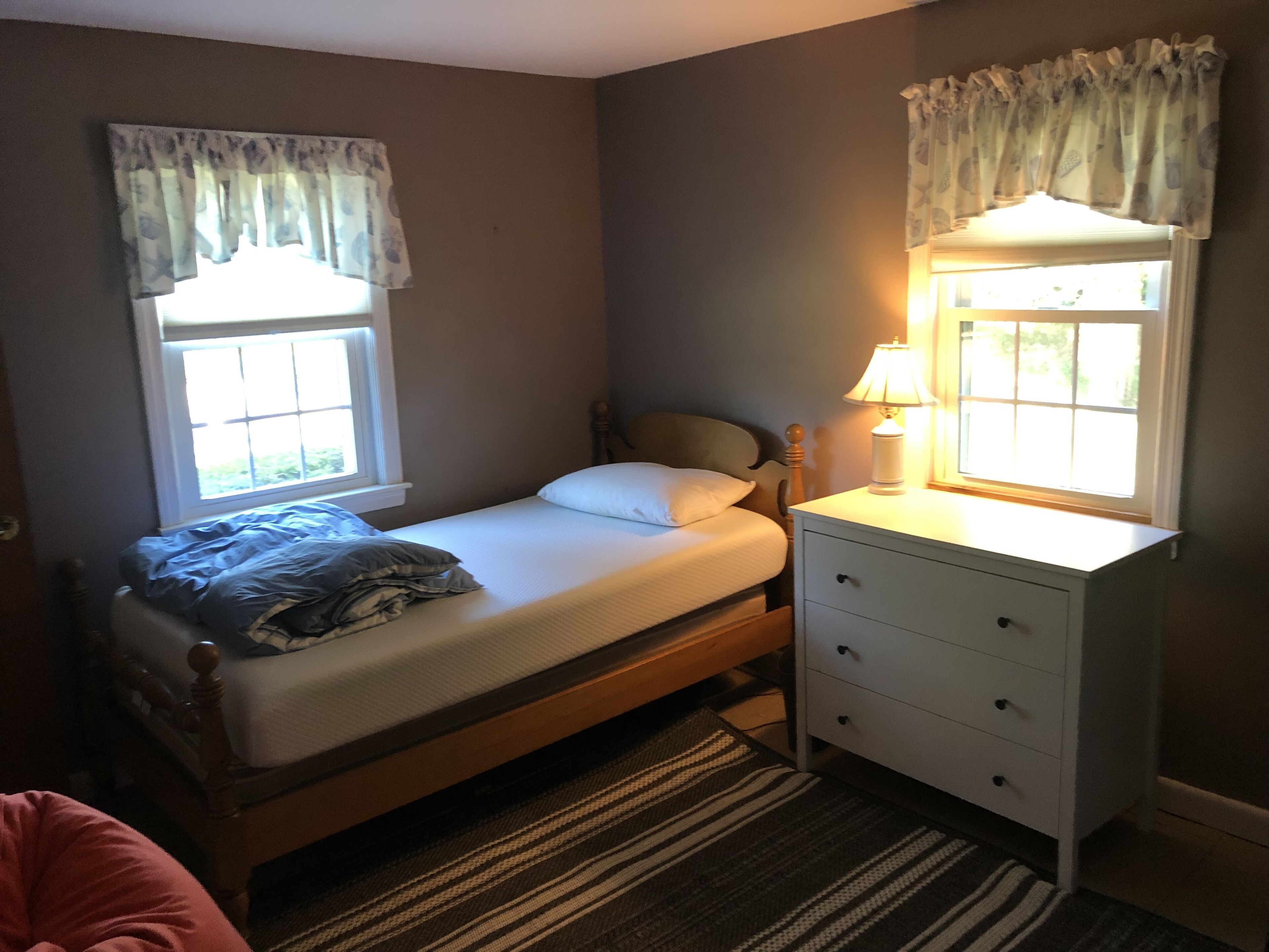 A bedroom with a single bed, a nightstand, a lamp, and a window with curtains.