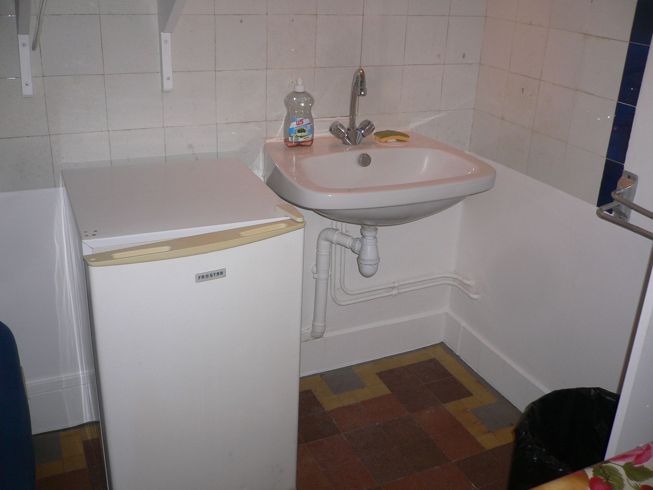 Une cuisine compacte avec un réfrigérateur blanc, un évier avec un robinet et un crédence carrelée.