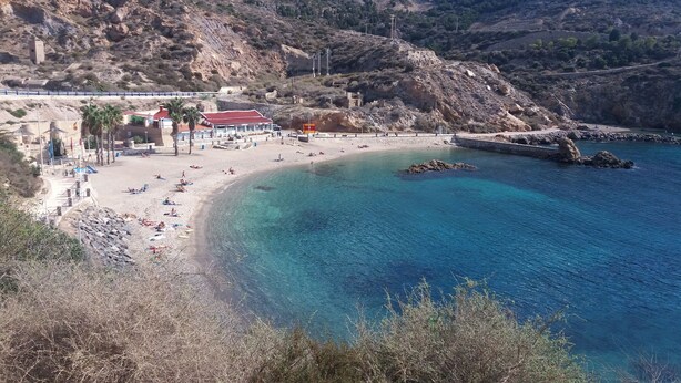 A beach with clear blue water, a sandy shore, and rocky hills in the background. -  Wonderful Top Floor Terrace, Distant seaview, Aircon, Free wifi, English TV (Villamartin)
