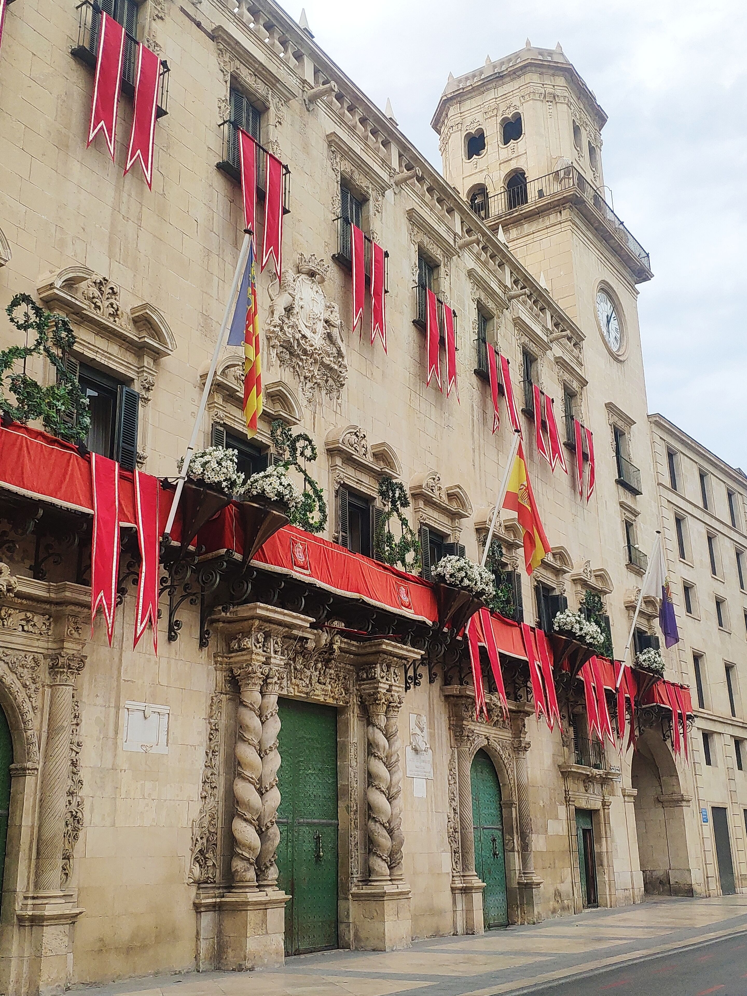 A historic building with ornate architecture, including a clock tower, multiple balconies with red awnings, and flags.