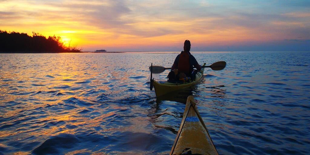 A person kayaking on a body of water during sunset.