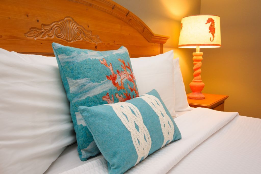Un lit bien fait, avec du linge de lit blanc, deux coussins décoratifs à motifs bleus et blancs, et une tête de lit en bois.