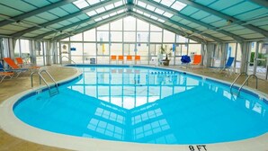 Una piscina interior con techo transparente, rodeada de sillas de descanso y suelo de baldosas.