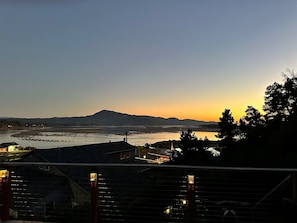Vista para o rio com montanha ao fundo, uma ponte e um edifício com telhado inclinado.