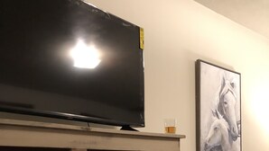 A living room with a flat-screen TV on a wooden stand, a framed picture on the wall, and a small glass of water on the stand.