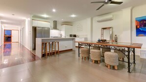 Een moderne keuken met een centraal eiland, barkrukken en een eettafel met rieten stoelen.