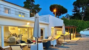 Un área de estar al aire libre moderna con mesas y sillas, una terraza de madera y un espacio cubierto con sombrillas.