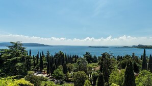 A coastal landscape with a clear view of the sea, a distant island, and a dense forest of tall trees. - Lake-view apartment Alloro (Gardone Riviera)