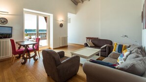 A living room with a wooden floor, a sofa, a coffee table, and a TV. There is a balcony with a view of the sea. - Lake-view apartment Alloro (Gardone Riviera)