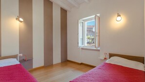 A room with two beds, a window with a view of the outside, and wall-mounted lights. - Lake-view apartment Alloro (Gardone Riviera)