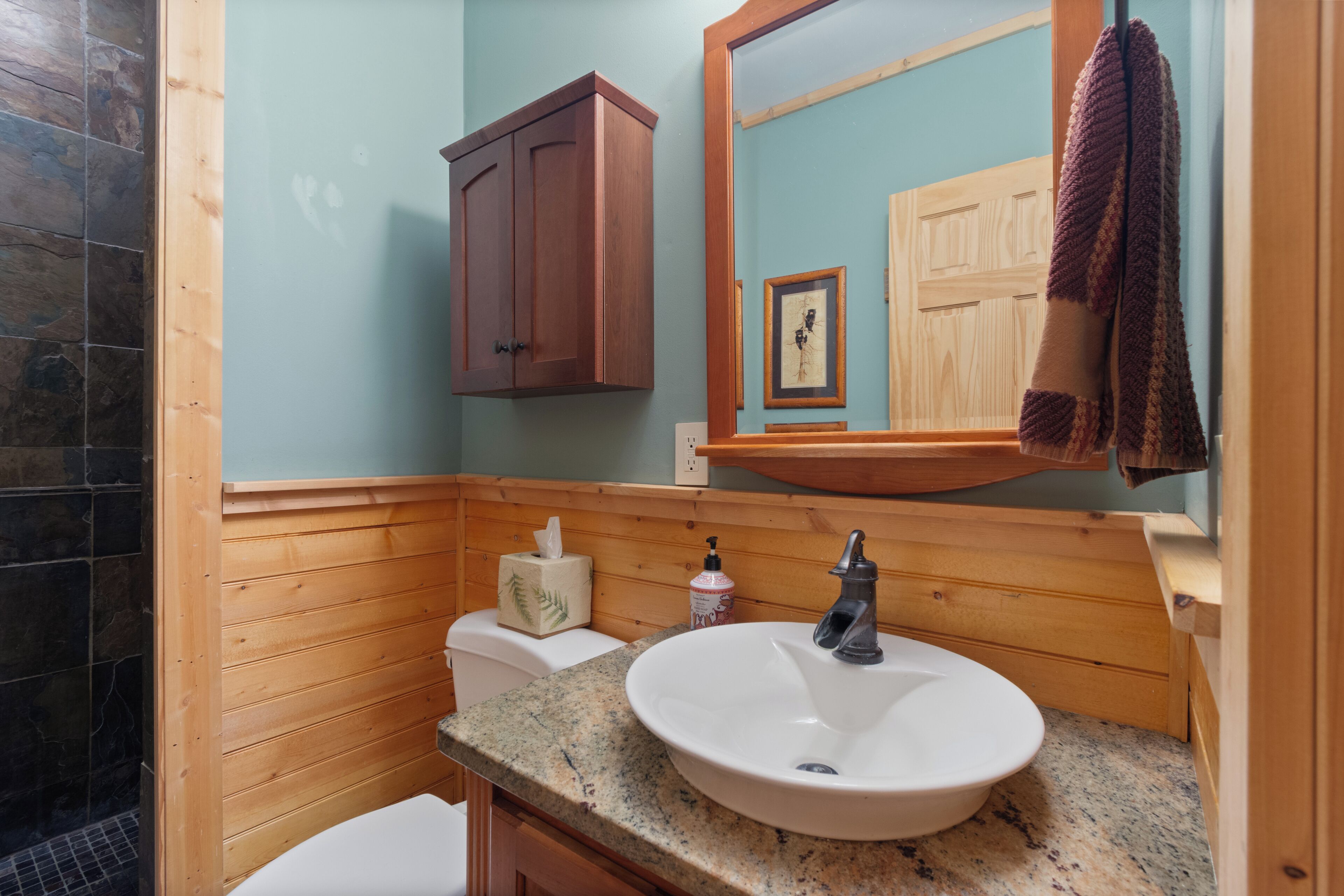 A bathroom with a wooden vanity, a sink, a mirror, and a towel hanging on the wall.