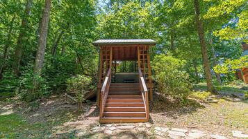 A wooden staircase leading to a covered wooden structure in a forested area.