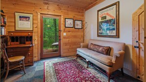 A wooden cabin interior with a sofa, a chair, a desk, and framed pictures on the walls.