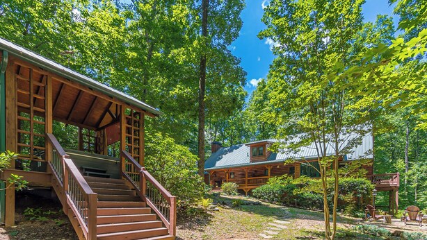 A rustic cabin with a wooden staircase leading to a porch, surrounded by dense trees and a clear sky.