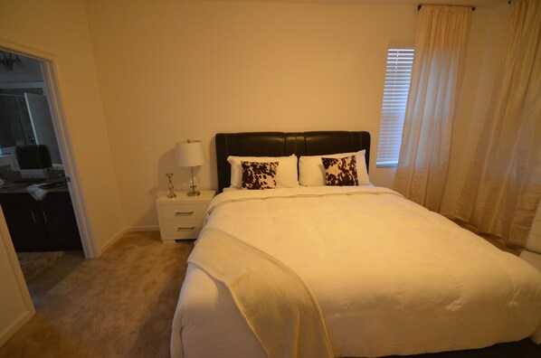 A bedroom with a large bed, a nightstand with a lamp, and a window with curtains.