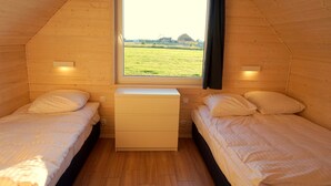 A small, cozy room with two single beds, a wooden dresser, and a window offering a view of a green field and distant buildings. - Cottages for families with children or guests who want to relax. (Sarbinowo)