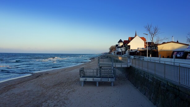 A coastal walkway with a stone wall, a metal railing, and a beach. - Cottages for families with children or guests who want to relax. (Sarbinowo)