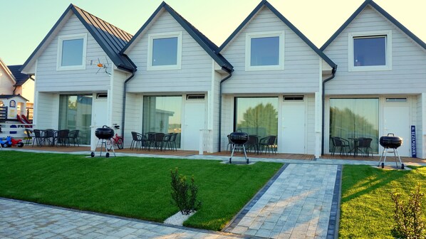 A modern house with a well-maintained lawn, outdoor seating, and barbecue grills.