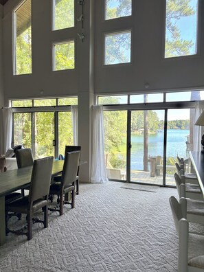 A spacious room with a large dining table, multiple chairs, and a view of a lake through large windows.