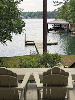 A lakeside view with a dock, a covered pavilion, and two Adirondack chairs.