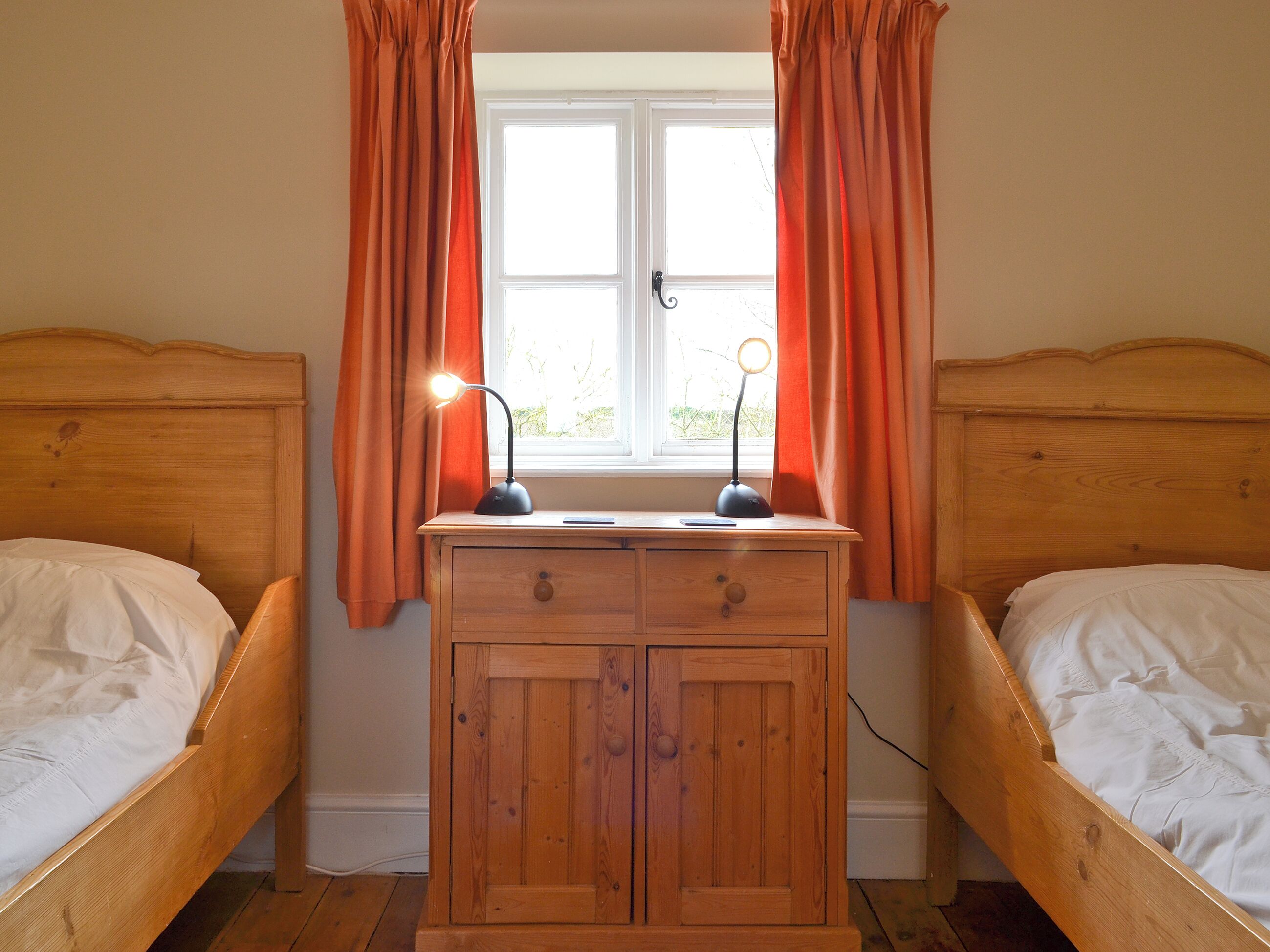 A bedroom with two wooden beds, a wooden dresser, and a window with curtains.