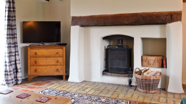 A cozy living room with a fireplace, wooden beams, a television on a wooden dresser, and a patterned rug. - 3 bedroom accommodation in South Acre (South Acre)